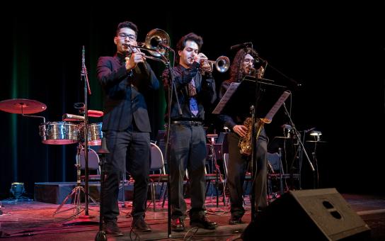 Three students on a performance stage in black shirts playing jazz horns.