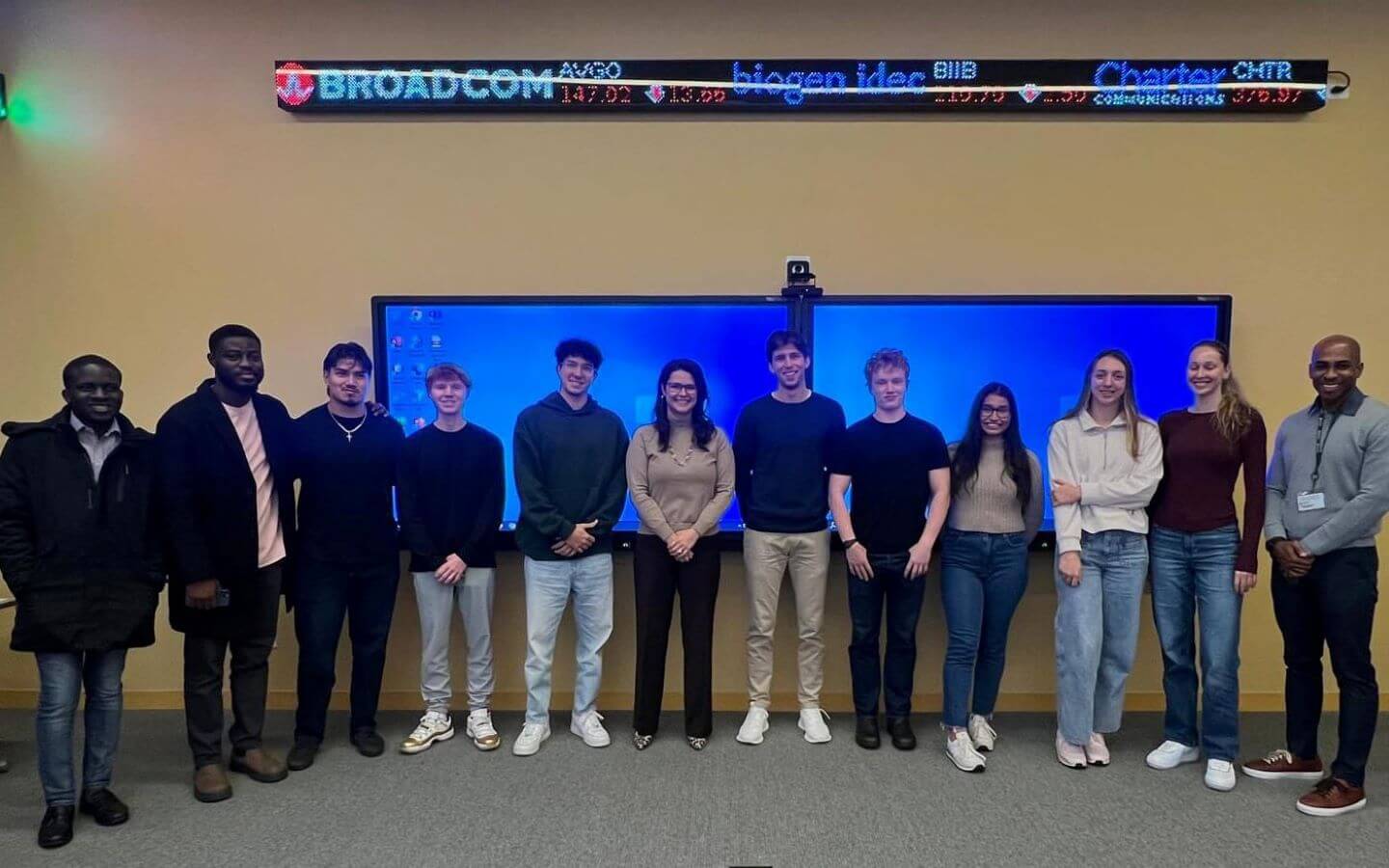 Group of students from the Investment Club standing in front of stock exchange ticker display with a guest financial advisor, Erica Marquez Avitia.