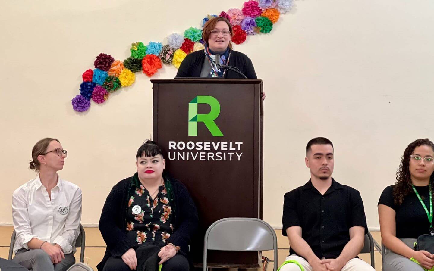 Meagan Jarmuz speaking at a podium behind students at the 2024 First-Gen Day celebration.