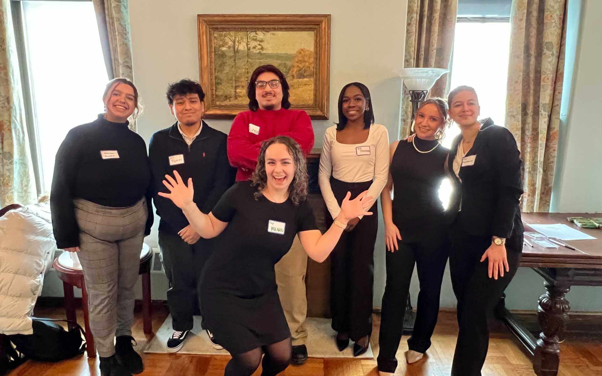 Eight honors student pose for a photo in the Sullivan room, wearing business attire and name tags.