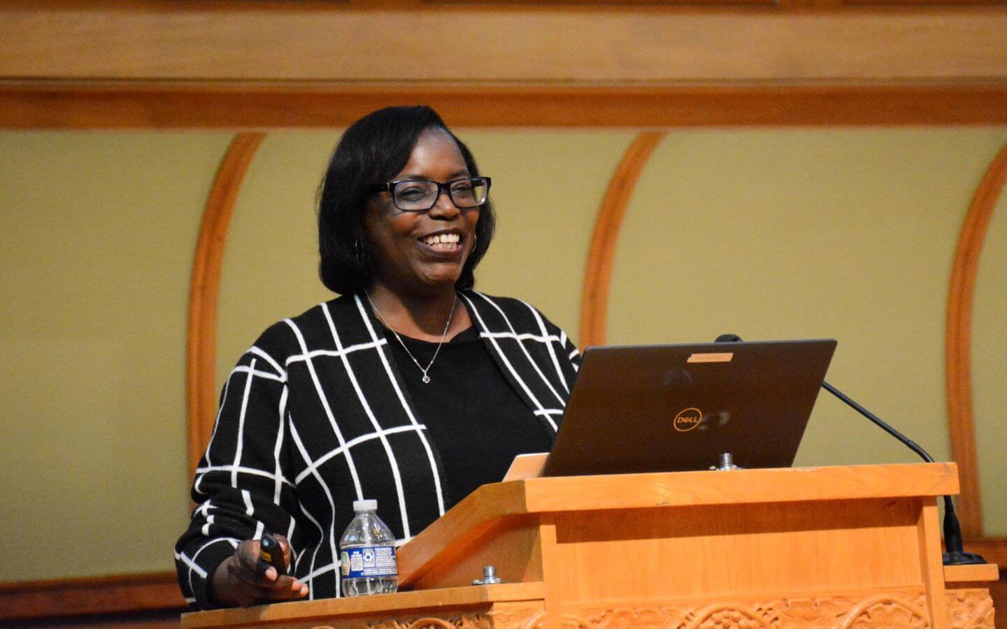 Alumnus, Melanie Hall, standing behind a podium with microphone and laptop