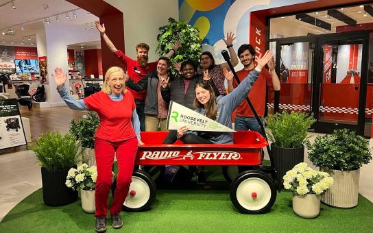 students holding a Roosevelt pennant while posing at the Radio Flyer offices