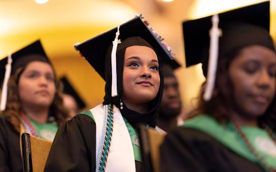 Graduating student in cap and gown looks hopefully into the air