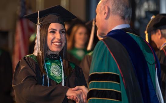 Smiling student shaking hands with President Ali Malekzadeh at Roosevelt Commencement